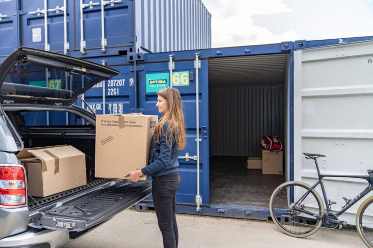 Woman loading cardboard boxes from a vehicle into a blue self storage container at Optima Self Store Corby.