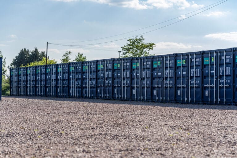 Long row of blue self storage containers at Optima Self Store Newark, with a gravel access area in front of the units.